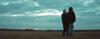 Genç bir adamla bir kadının sonbahar sahasında yürürken çekilmiş bir fotoğraf.