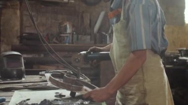 Demircilik yaparken önlüklü bir demirci, kesme tekerleği kullanıyor.