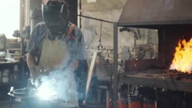 Demirci, koruyucu miğferini takmış demir ocağı ve kaynak demiriyle açık ateş başında demircide çalışırken...