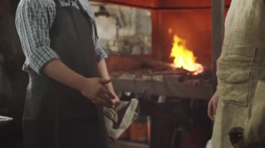 İki demircinin atölyede el sıkışarak birbirlerini selamladıkları orta bölüm çekimi.