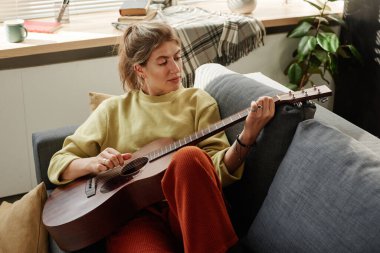 Kadın evde gitar çalmayı öğreniyor.