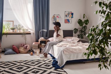 Kadın yatağın üstüne oturan baş ağrısı ile