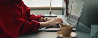 Genç beyaz kadının klavyeye yazı yazarken ve ofisteki masada interneti karıştırırken laptopunu kullanırken görüntüyü kaldır.