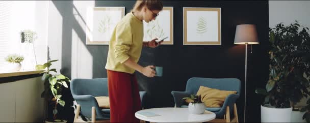 Jonge Vrouw Loopt Moderne Kamer Zit Een Fauteuil Drinkt Koffie — Stockvideo