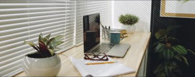 Ev penceresinin pervazına dizüstü bilgisayarlar, bitkiler, kağıtlar ve kupalarla rahat iş yerinin arkasını kapat
