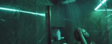 Genç Afrikalı Amerikalı kadın yeşil mermer banyoda duş alıyor.