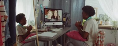 Genç Afrikalı Amerikalı kadın evde oturmuş bilgisayardan iki kız arkadaşıyla sohbet ediyor.