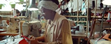 Genç Afrikalı Amerikalı kadın telefonda mesajlaşıyor ve ayakkabı yapma atölyesinde masasında gülümsüyor.