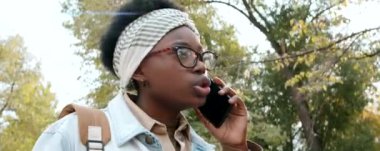 Genç Afrikalı Amerikalı bir kadının parkta yürürken cep telefonuyla konuştuğu düşük açılı bir görüntü.