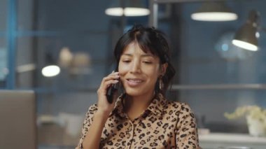 Güzel İspanyol iş kadını ofiste geç saatlere kadar çalışırken cep telefonuyla konuşuyor.