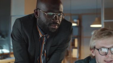 Kafkasyalı ve Afrikalı Amerikalı iş adamları gece ofisinde çalışırken bilgisayar ekranında bir şey tartışıyorlar.