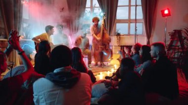 İnsanlar onları alkışlarken stüdyoda canlı konser veren, neon ışıklı ve dumanlı çok ırklı erkek müzisyenlerin görüntülerini yakınlaştırın.