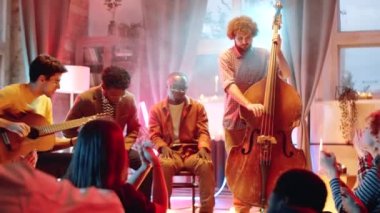 Genç, çok ırklı erkek müzisyenler gitar ve bas çalıyorlar ve canlı ev konserinde dumanlı ve neon ışıklı bir şarkı söylüyorlar.