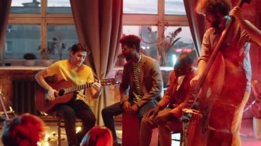 Stüdyoda neon ışıklı küçük bir atmosfer konserinde şarkı söyleyen ve çalan çok ırklı bir grup genç müzisyen.