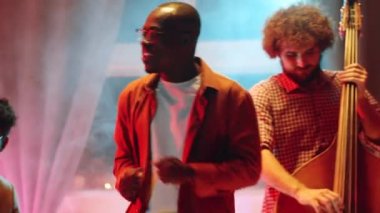 Neşeli Afrikalı Amerikalı adam müzik grubuyla konser verirken dans ediyor ve şarkı söylüyor.