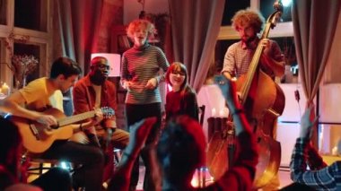 İki beyaz kadın ve Afrikalı Amerikalı erkek, stüdyoda neon ışıklı bir konser verirken gitar ve bas gitar eşliğinde birlikte şarkı söylüyorlar.