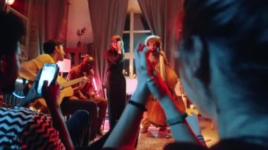 İnsanlar konser sırasında müzik grubunu alkışlıyor ve telefonla fotoğraf çekiyor.