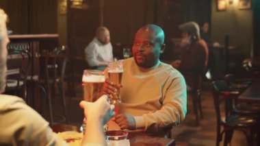 İki adamın barda oturup bardaklarını birayla tokuşturup içerken yavaş çekim çekimleri.