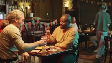 Etnik çeşitliliğe sahip yetişkin erkek arkadaşlarının geceyi barda bira içerek ve sohbet ederek geçirdikleri el kamerası görüntüleri.