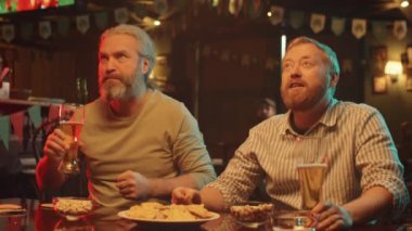 İki olgun beyaz adamın gastrobar 'da futbol maçı izlediği orta yavaş görüntüler.