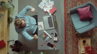 Erkek moda tasarımcısının dizüstü bilgisayar ekranına bakıp heyecanla bağırması ve ofisteki başarıyı kutlaması.