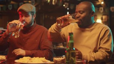 Afro-Amerikalı ve beyaz erkekler masaya oturup bardaklarını birayla tokuşturup bir şeyler hakkında konuşuyorlar.