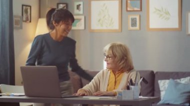 Genç öğretmen, tekerlekli sandalyede oturan yaşlı kadına laptopla masaya oturması için yardım ediyor sonra da derse başlıyor.