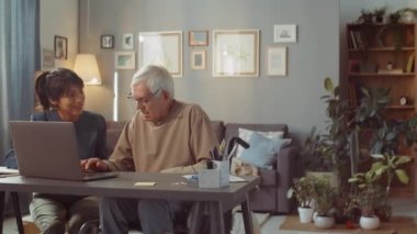 Genç bir kadın, internet sörfü ve işi için dizüstü bilgisayar kullanmayı öğrenmesine yardım etmek için evde yaşlı bir adamla vakit geçiriyor.