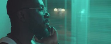 Afro-Amerikalı bir adam evinin penceresinin önünde dikiliyor ve geceleri cep telefonuyla konuşuyor.