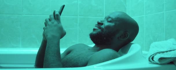 Uomo Afroamericano Sdraiato Nella Vasca Bagno Messaggistica Sul Telefono Cellulare — Video Stock