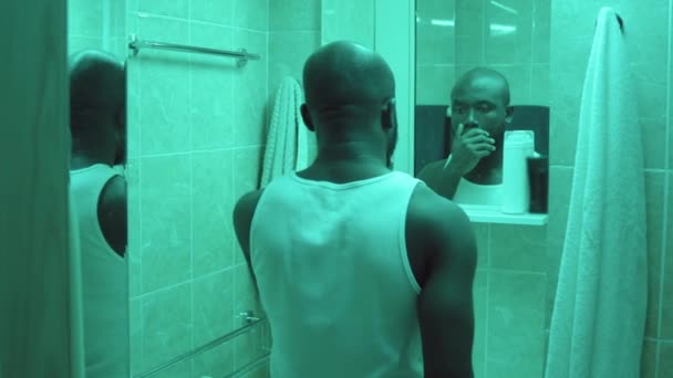 鏡を見て歯を磨くアフリカ系アメリカ人男性が家でバスルームを歩いている姿を — ストック動画