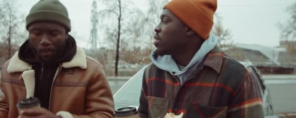 2人の若いアフリカ系アメリカ人男性がファーストフードを食べ コーヒーを飲み 車で屋外でチャットする — ストック動画