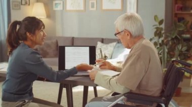 Genç bir kadının yaşlı bir adamla çalışırken çekilmiş yatay bir fotoğrafı. Bireysel ders sırasında ona konuyu açıklıyor.