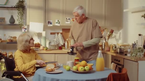 一对中年夫妇在厨房度过了一个上午 残疾妇女在为三明治切面包 她心爱的丈夫在为她倒咖啡 — 图库视频影像