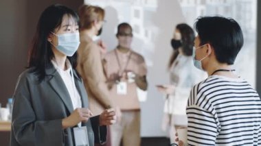 Korumacı yüz maskesi takmış iki Asyalı kadın meslektaşı covid-19 salgını zamanında iş etkinliği hakkında konuşuyor.