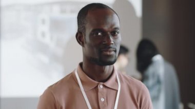 Rozetli neşeli siyahi adamın portresi kameraya bakıyor ve iş konferansında gülümsüyor.