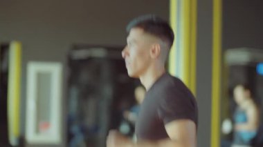 Spor kıyafetli genç bir sporcunun spor salonundaki koşu bandında koşarken yan görüntüsünü kaldır.