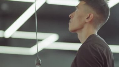 Spor kıyafetli bir adamın spor salonunda kablo makinesiyle egzersiz yaparken ayakta durduğu yakın çekim.