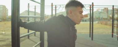 Spor kıyafetli genç adam antrenman parkında antrenman yapmadan önce omuzlarını geriyor.