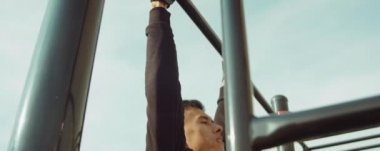 Spor giyimli genç bir sporcunun oyun parkında antrenman yaparken barfiks çekerken ki arkası.