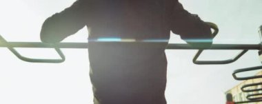 Spor giyimli bir adamın sabah antrenman yaparken bara yürüyüp barfiks çekerken ki görüntüsü.