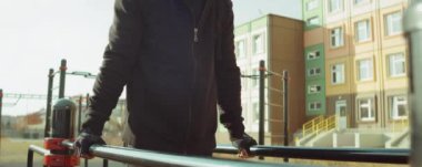 Paralel barlara dalan güçlü bir adamın dışarıda oyun parkında antrenman yaparken ki görüntüsü.