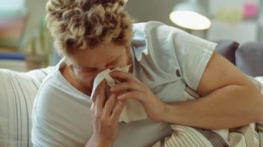 Hasta adam evdeki kanepede uzanıyor, peçeteye hapşırıyor ve soğuk algınlığı çekerken burun spreyi kullanıyor.