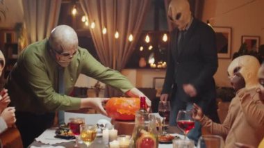Kafatası ve uzaylı maskeleri takmış neşeli çoklu etnik arkadaş grubu evde Cadılar Bayramı partisi yaparken dans ediyor, gülümsüyor ve maytap tutuyorlar.