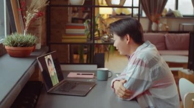 Genç Asyalı kadın evde oturuyor ve kız arkadaşıyla bilgisayarda konuşuyor.