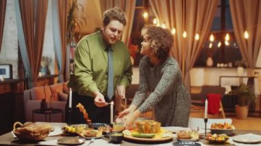 Beyaz bir erkek ve siyah bir kadın akşamları evde yemek masası hazırlayıp mum yakıyor.