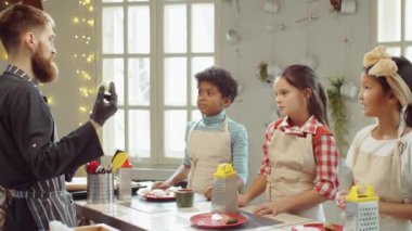 Şef, aşçılık kursu sırasında elinde peynirle bir grup çoklu etnik çocuğa yemek tarifi veriyor.