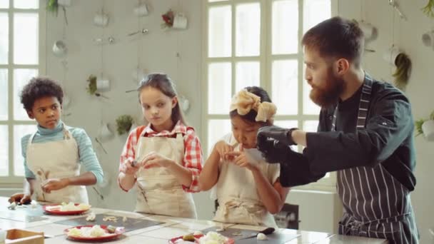 戴着手套和围裙的男厨师在烹饪大师课上教多民族小孩如何切领头羊 — 图库视频影像