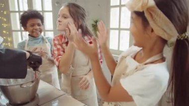 Oyuncu küçük çocuklar yüzlerine un sürüp gülerken şef ana yemek kursu sırasında malzemeleri kaseye karıştırıyor.