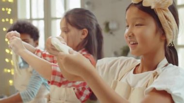 Küçük Asyalı kız yemek pişirmeye hazırlanıyor, gülümsüyor ve çocuklar yemek yaparken bir şeyler anlatıyor.